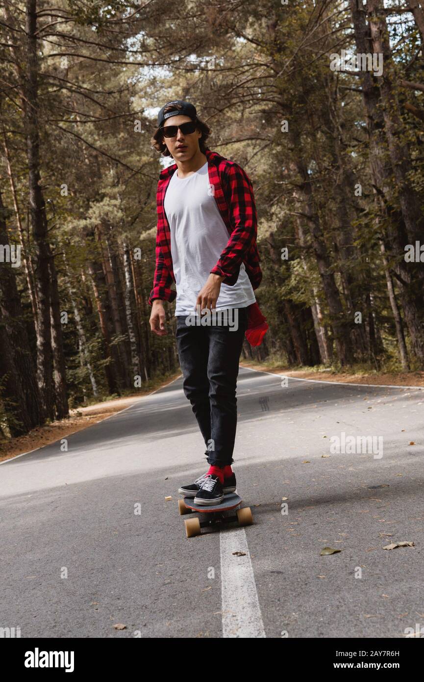 Un joven hipster en una gorra y camisa de cuadros está montando su longboard  en una carretera de campo en el bosque Fotografía de stock - Alamy