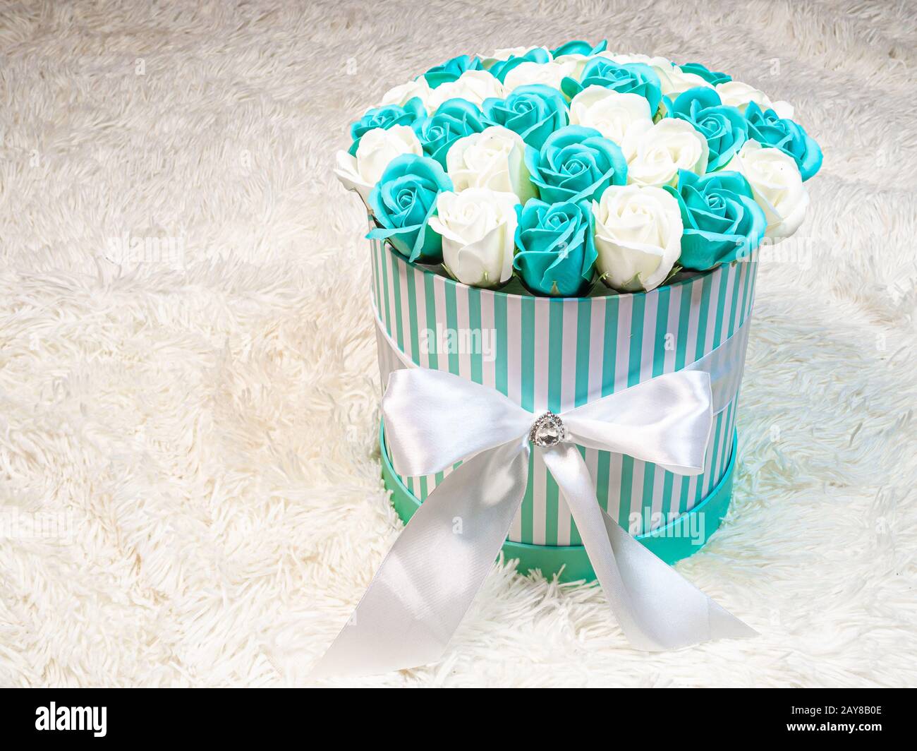 Rosas blancas y verdes-azules en una caja cilíndrica de regalo atada con  una cinta blanca sobre un fondo de piel blanca. Arreglo floral festivo para  da de San Valentín Fotografía de stock -