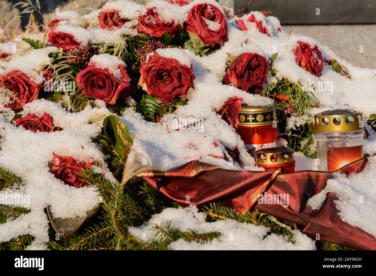 Arreglo con rosas rojas cubiertas de nieve en la tumba con velas graves - servicio funerario Foto de stock