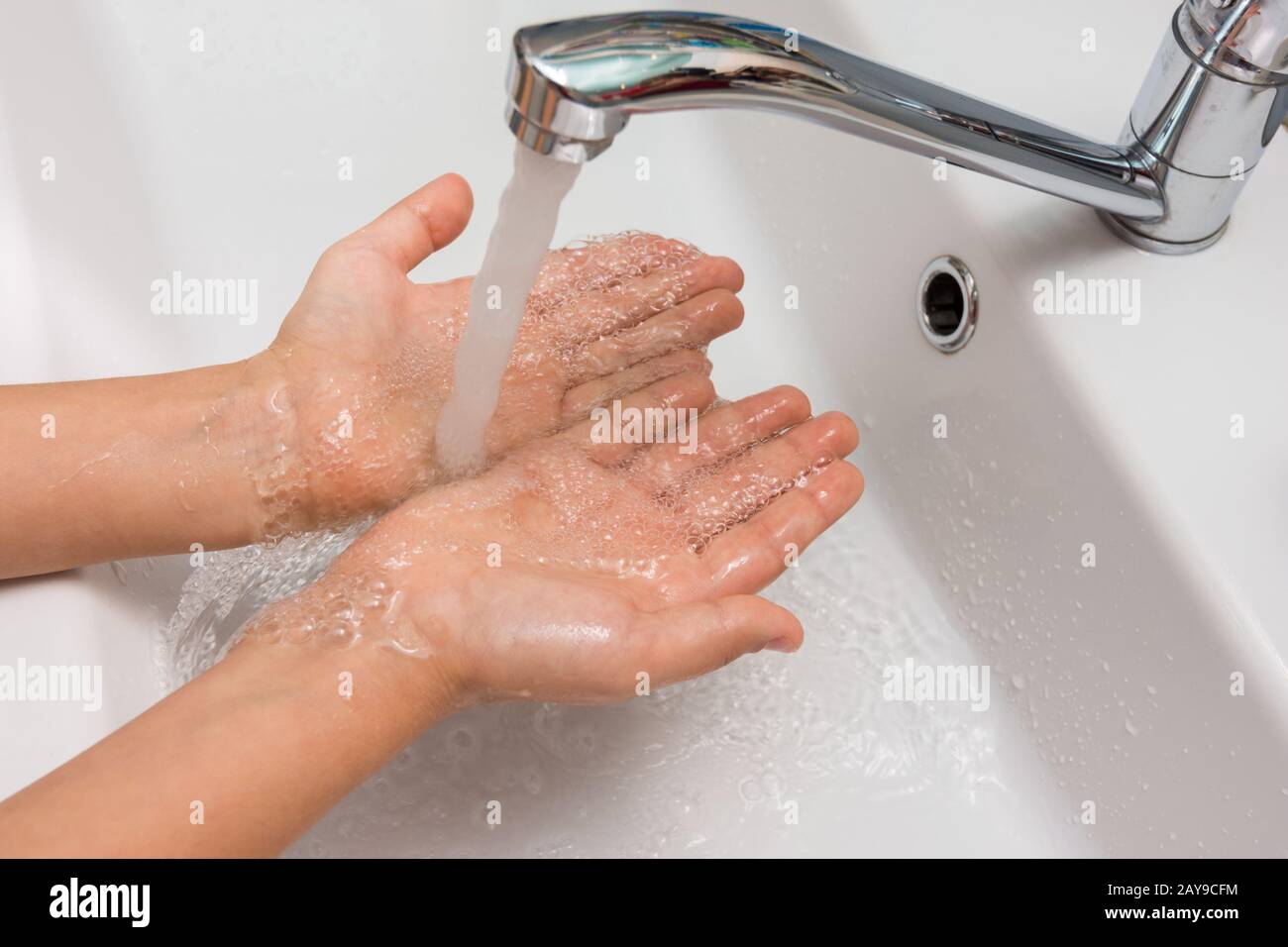 Las manos de los niños, bajo un fuerte chorro de agua desde el mezclador en el baño Foto de stock