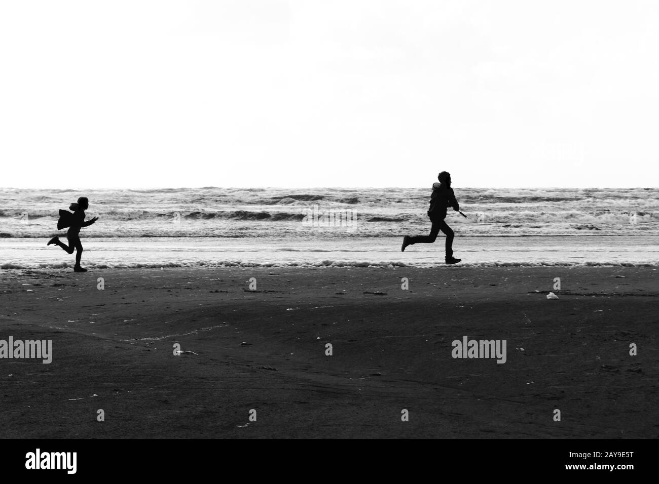 Siluetas de un hermano y una hermana corriendo salvaje y libre en la playa Foto de stock