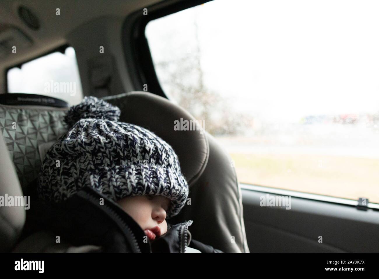 El niño que lleva sombrero de invierno duerme mientras está en el asiento del coche dentro del monovolumen Foto de stock