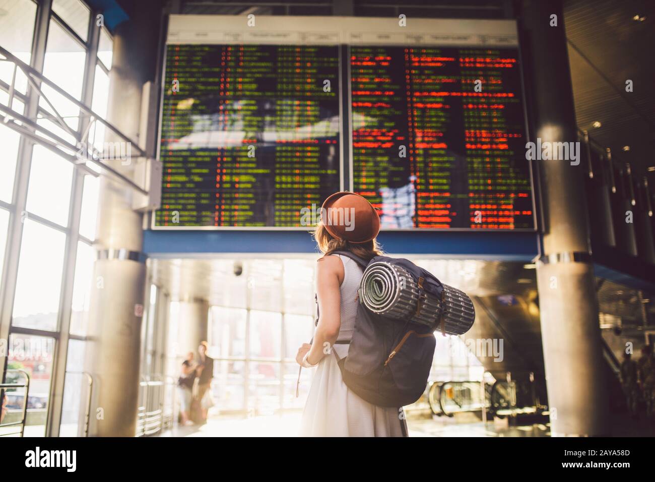 Viaje temático transporte público. Mujer joven de pie con espalda vestida y sombrero detrás de mochila y equipo de camping para dormir Foto de stock