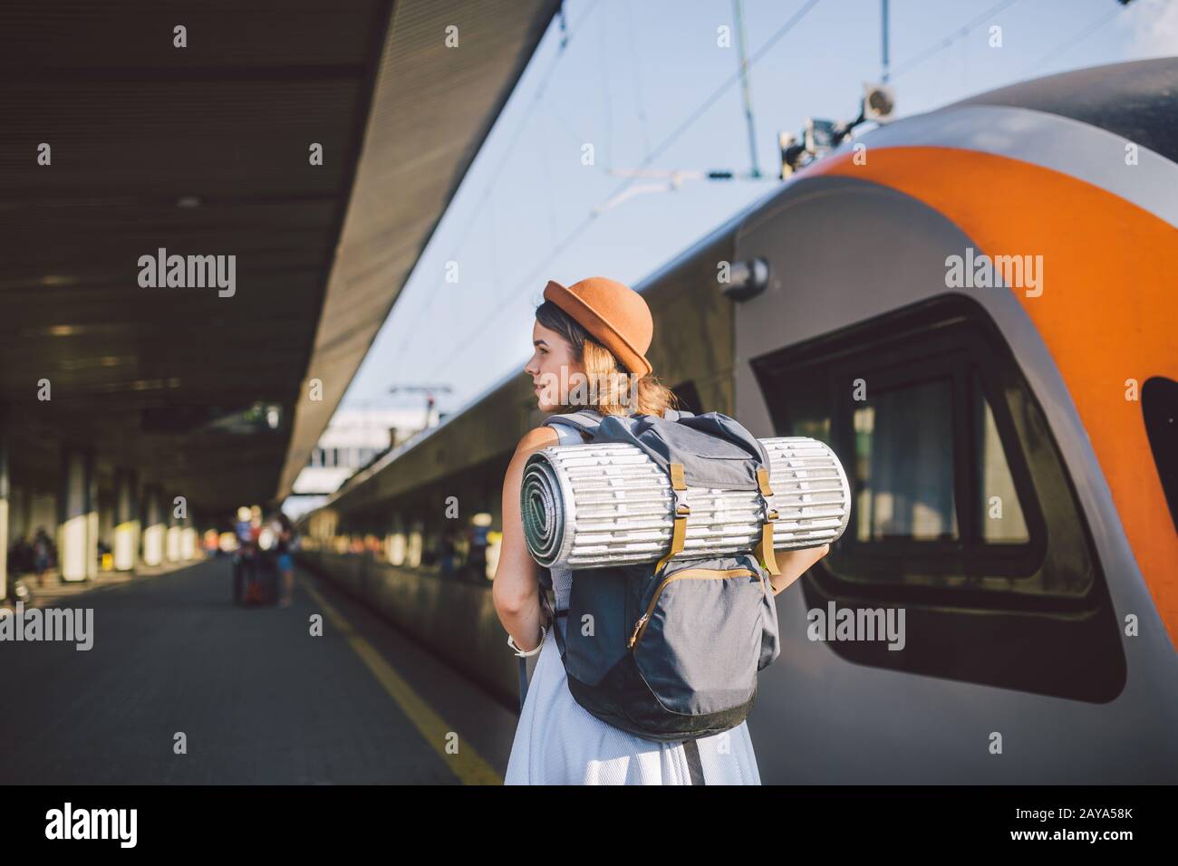 Tema de transporte y viajes. Mujer caucásica joven de pie en la plataforma de la estación de tren cerca de los trenes de fondo de tren con Foto de stock