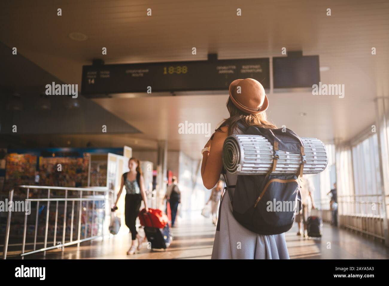 Viaje temático transporte público. Mujer joven de pie con espalda vestida y sombrero detrás de mochila y equipo de camping para dormir Foto de stock