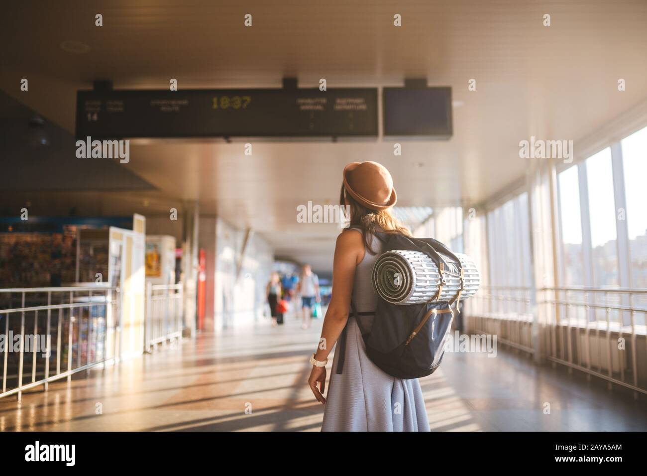 Viaje temático transporte público. Mujer joven de pie con espalda vestida y sombrero detrás de mochila y equipo de camping para dormir Foto de stock