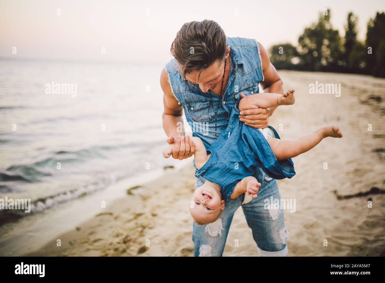 Tema la paternidad y el descanso con un niño en el mar. Joven guapo padre caucásico juega juega disfruta tirar en brazos a su hijo Foto de stock