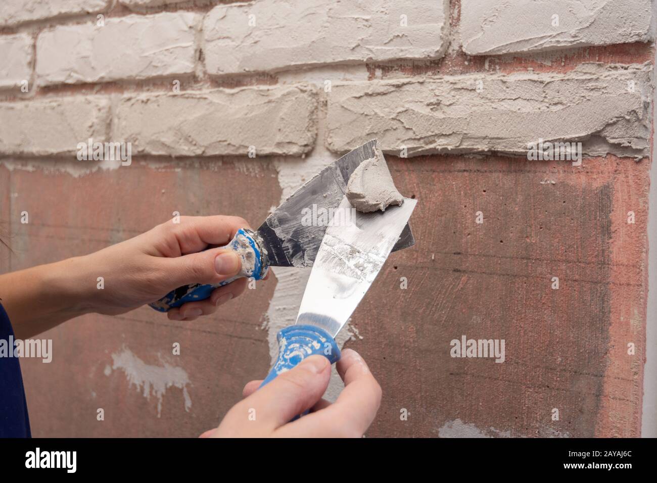 Albañil trabaja con dos espátulas de aplicar el yeso de la pared Foto de stock