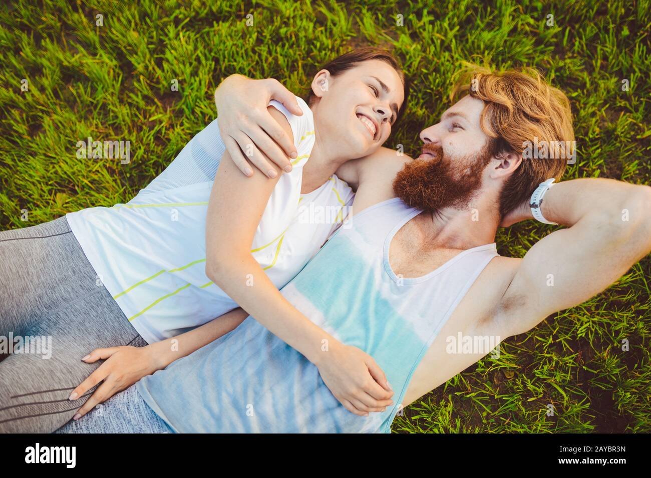 El tema es el deporte y un estilo de vida saludable. Un joven y una pareja de mujeres están descansando sobre sus espaldas en la hierba verde, un césped Foto de stock