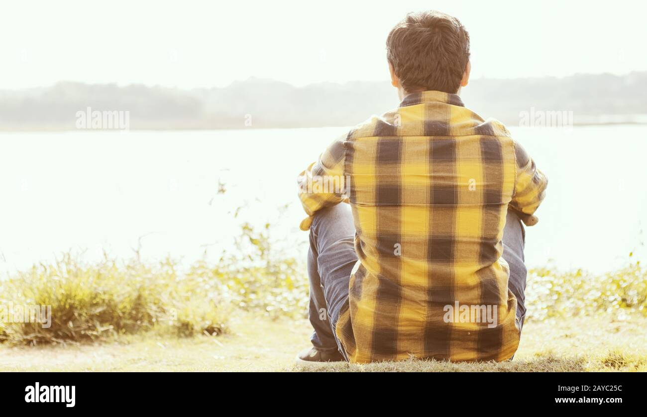 Un hombre solitario sentado frente al lago En un día soleado - Concepto de soledad, romper, solo y solo. Foto de stock
