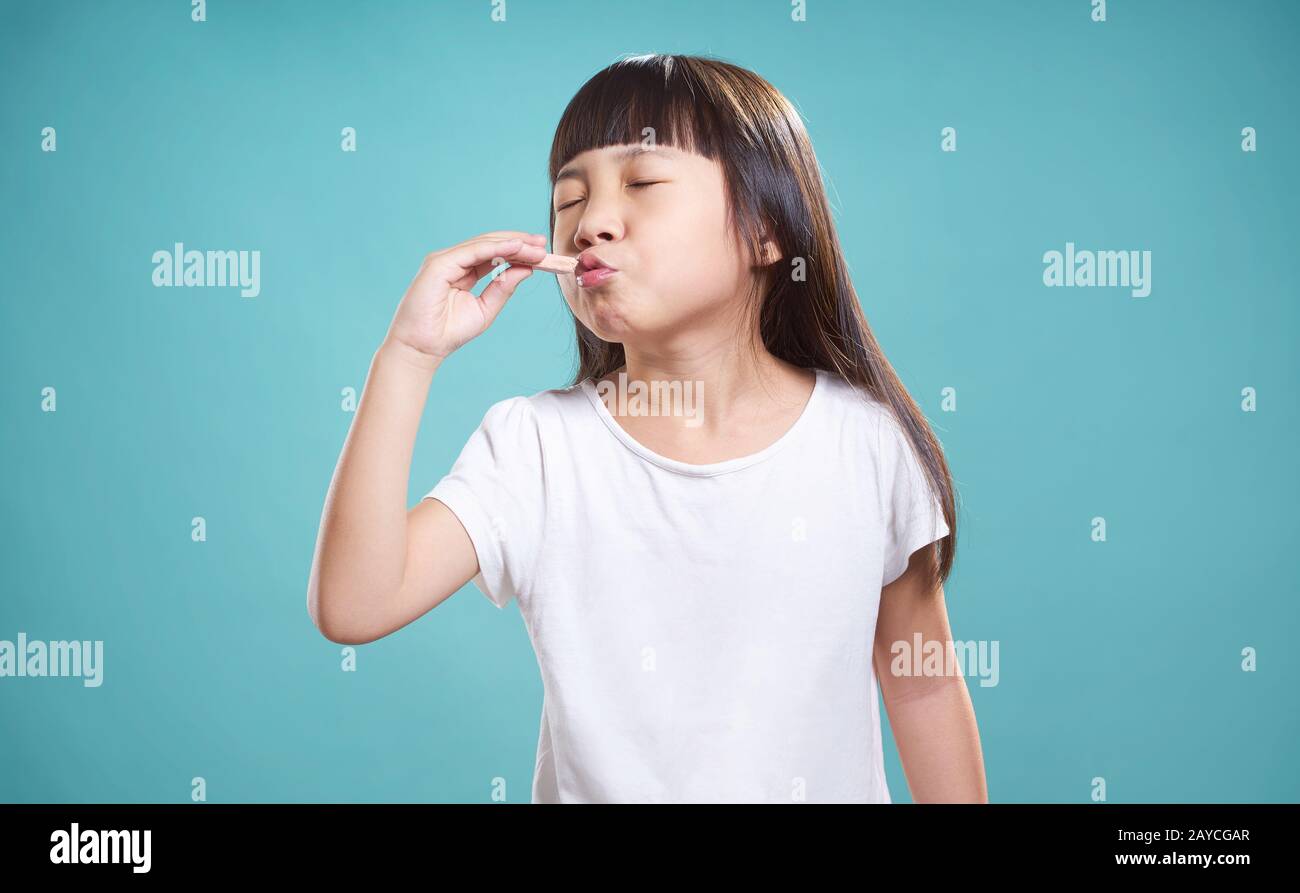 Close Up retrato de asian poco feliz chica con buen sabor chocolate . aislado sobre fondo azul claro . Foto de stock