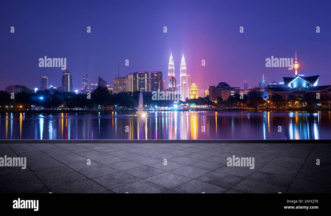 Vista nocturna de la ciudad de Kuala Lumpur con un impresionante reflejo en el agua y piso cuadrado vacío de concreto Foto de stock