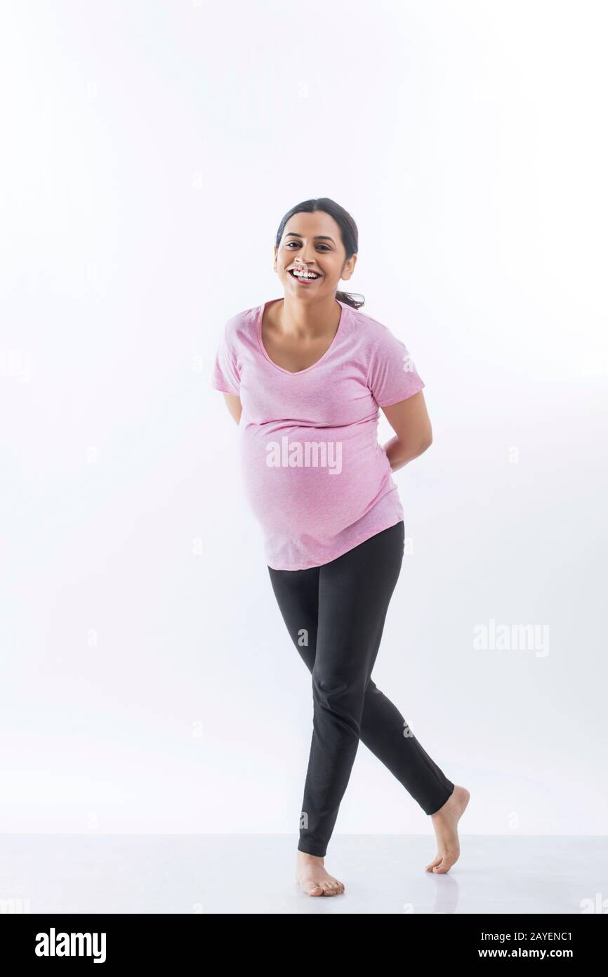 Alegre mujer embarazada de pie con sus piernas cruzadas y sonriendo. Foto de stock