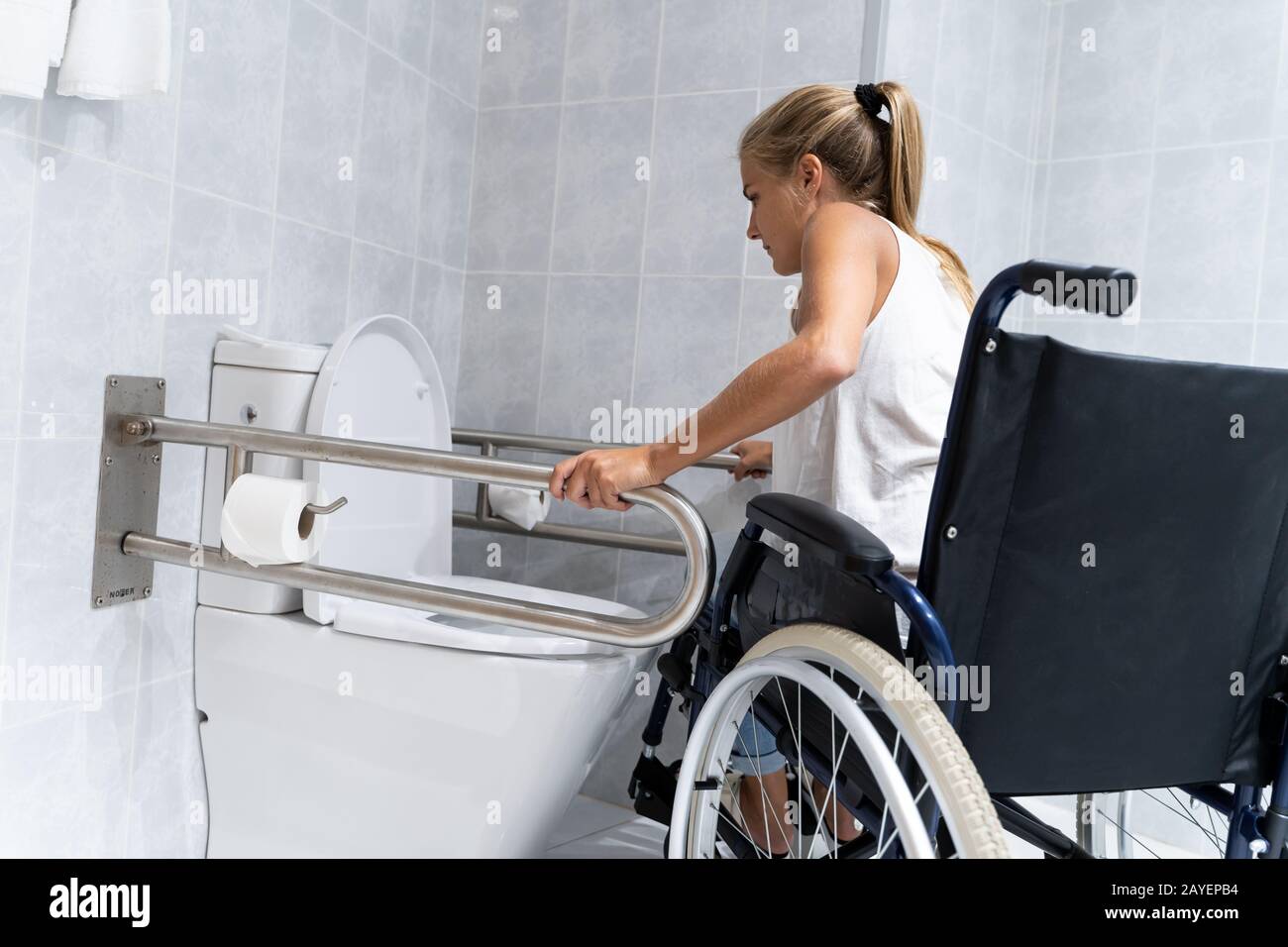 Chica rubia sujetándose a los rieles en el baño tratando de levantarse con  sus brazos de una silla de ruedas para ir al baño Fotografía de stock -  Alamy