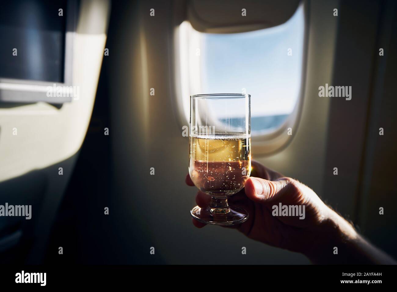Bearing durante el vuelo. Hombre sosteniendo una copa de vino espumoso contra la ventana del avión. Foto de stock