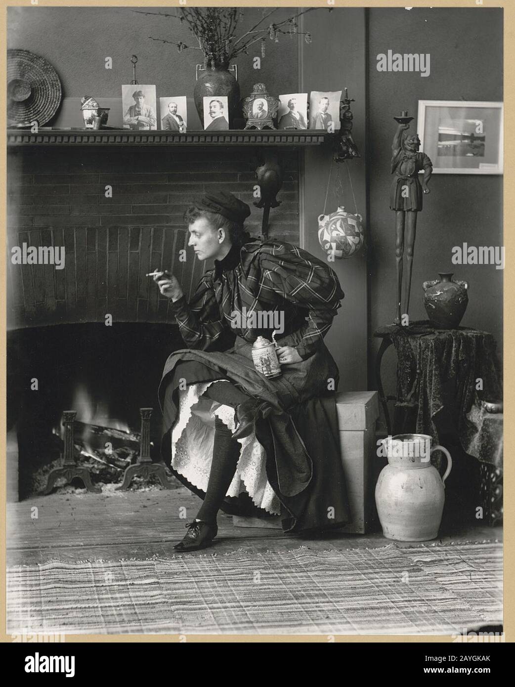Frances Benjamin Johnston, retrato de longitud completa, sentado frente a la chimenea, mirando hacia la izquierda, sosteniendo un cigarrillo en una mano y una cerveza stein en la otra, en su estudio de Washington, D.C. Foto de stock