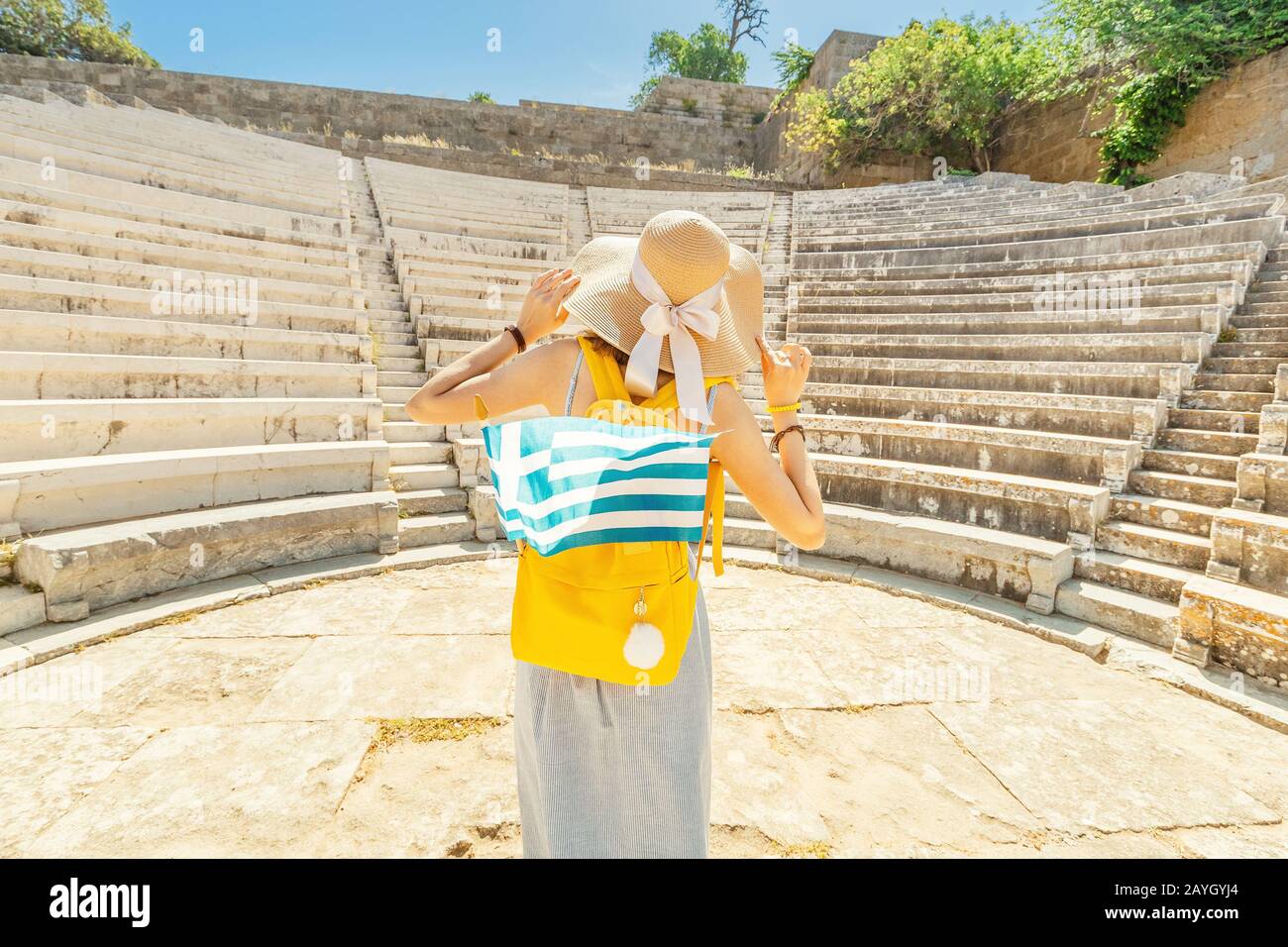 Turista asiática que viaja en las ruinas de una antigua Acrópolis o el anfiteatro con bandera griega. Concepto de jóvenes viajeros y estudiantes activos Foto de stock