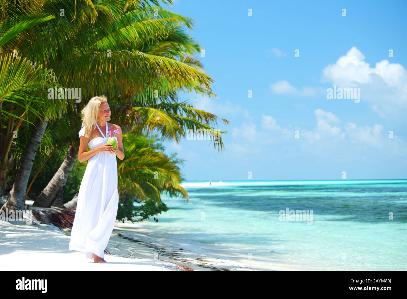Mujer con un largo vestido blanco caminando en la playa tropical con  palmeras que sostienen un cóctel de coco y sonriendo Fotografía de stock -  Alamy