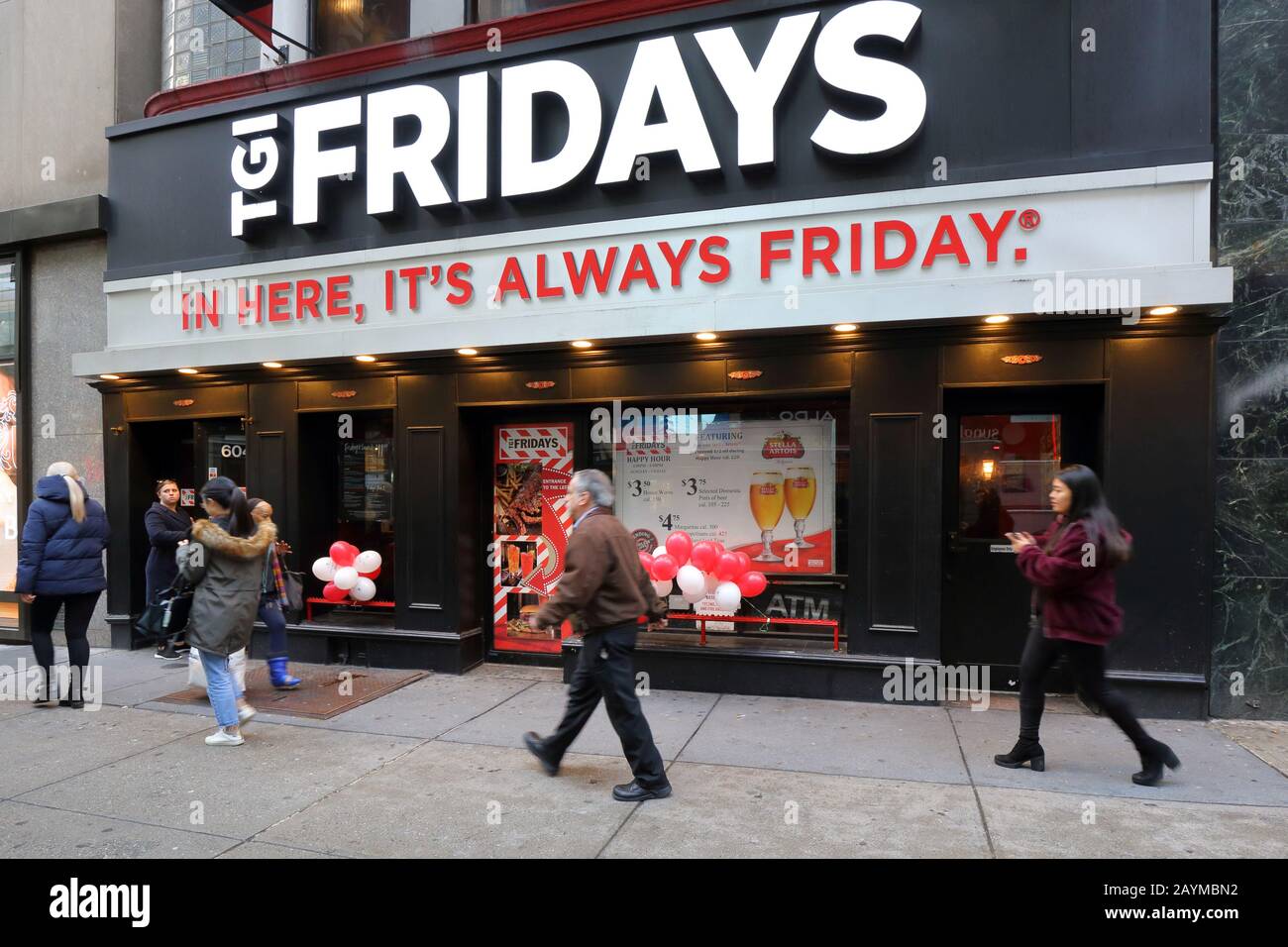La gente caminando pasando un restaurante temático de la cadena TGI Fridays happy hour en 604 5th Ave en Midtown Manhattan, Nueva York, NY. Foto de stock