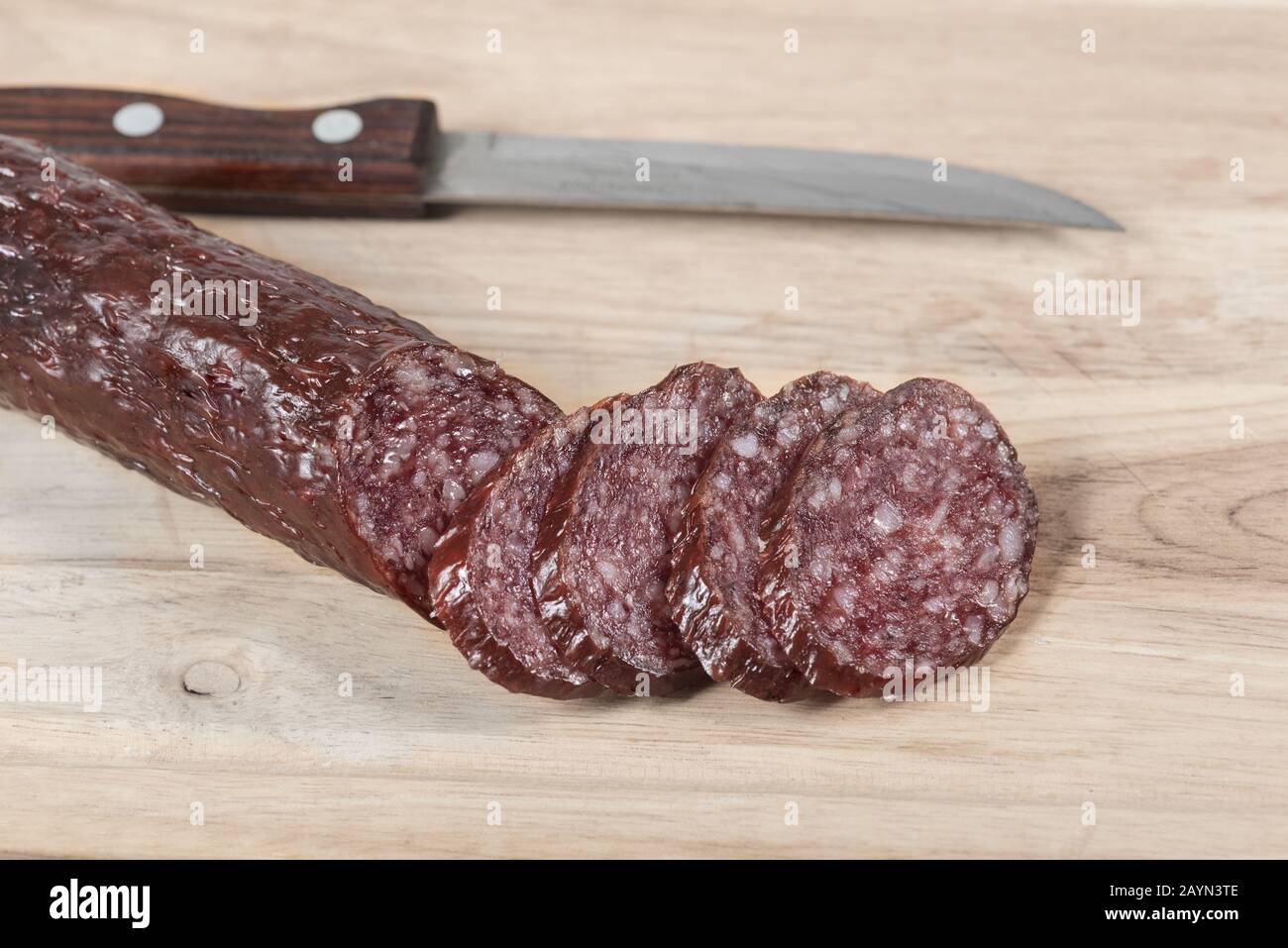 Barra de salchichas de salami en grasa seca y cuchillo en tabla de madera con rodajas. Primer plano. Vista superior Foto de stock
