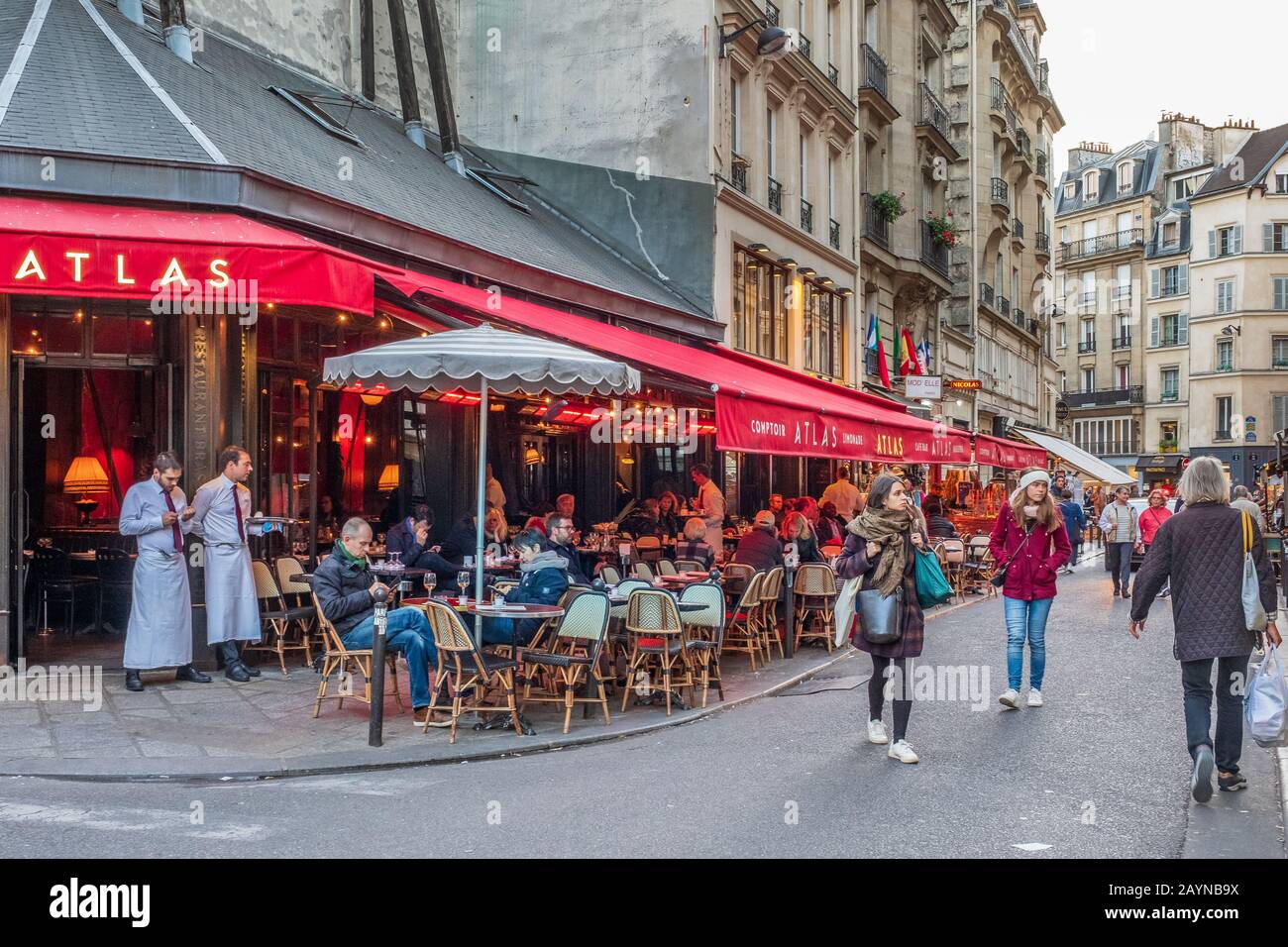 Una escena callejera en París con residentes sentados fuera en un restaurante y gente caminando por la calle Foto de stock