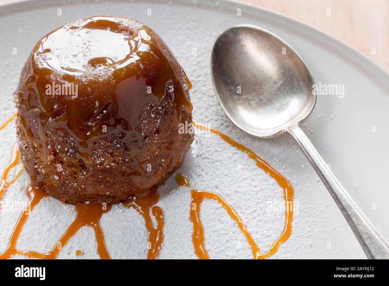 Pudding de toffee pegajoso en un plato blanco de azúcar espolvoreado con salsa de caramelo con una cuchara Foto de stock