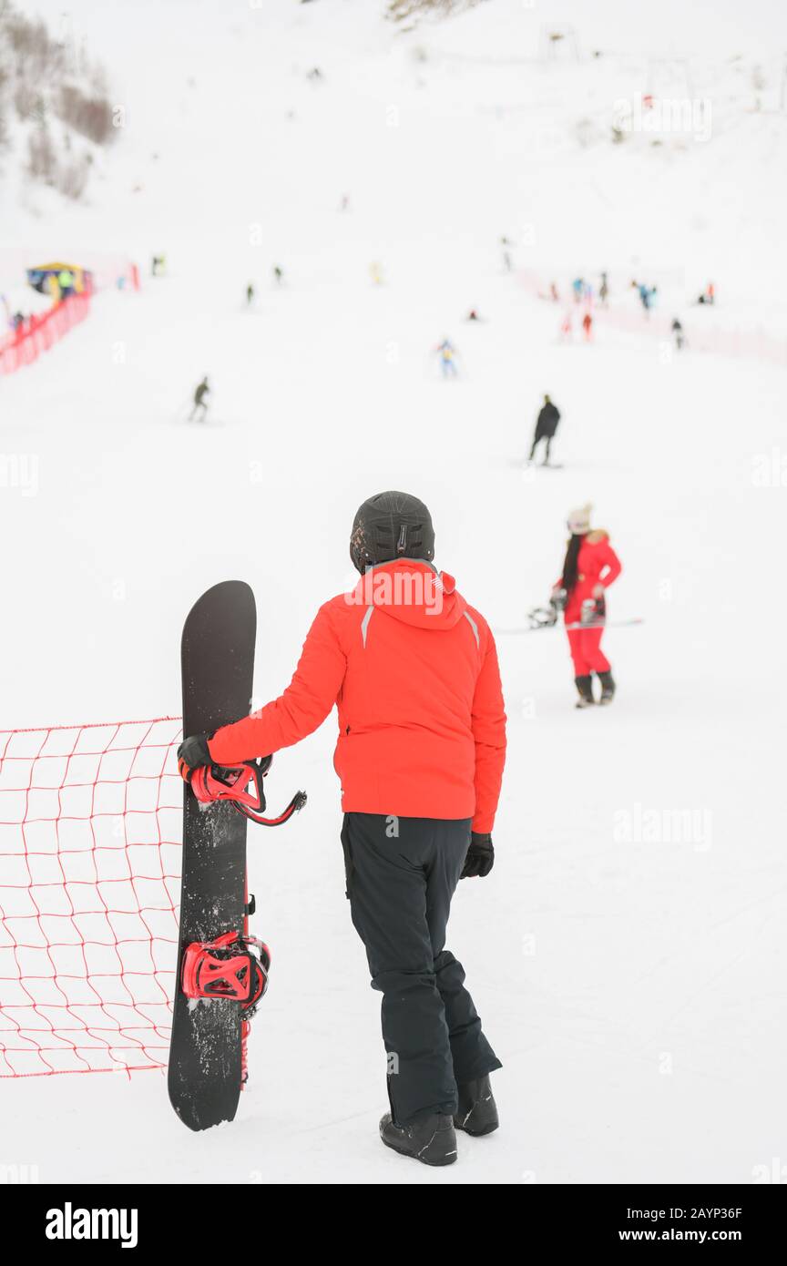 hombre en casco negro con ropa deportiva de invierno sosteniendo snowboard  mirando a la montaña de nieve con esquiadores y snowboarder niña con ropa  roja Fotografía de stock - Alamy