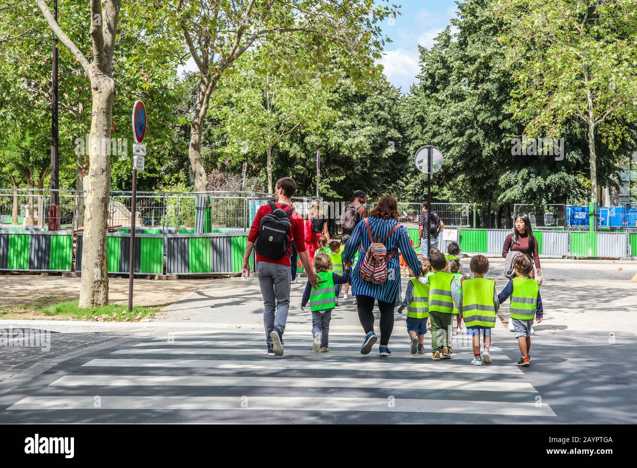 Niños pequeños en chaquetas de alta visibilidad acompañados por adultos a través de un cruce de cebra en París, Francia, Europa Foto de stock