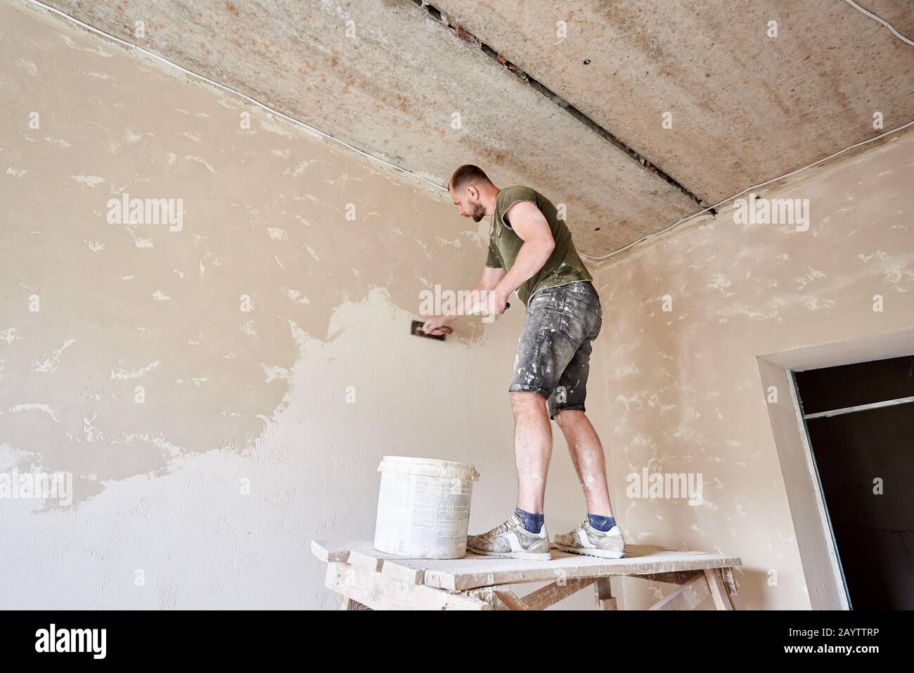 joven hombre utilizando espátula y enlucido de pared con blanco