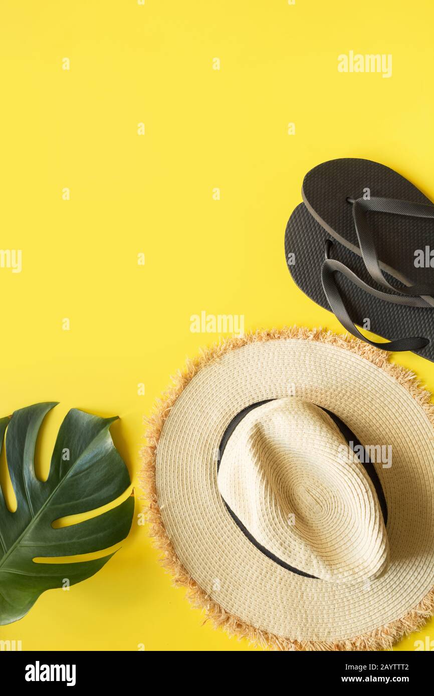 Sombrero de paja de playa, chanclas y monstera como frontera. Vacaciones de verano de fondo sobre amarillo. Vista desde arriba. Espacio para texto. Formato vertical. Foto de stock
