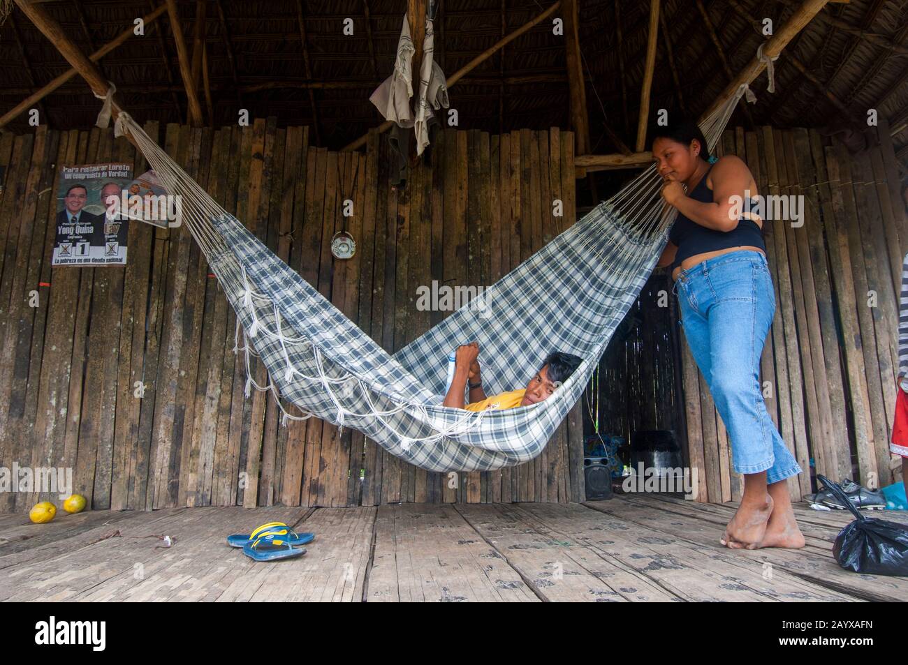 Una pareja en una hamaca en una casa sobre pilotes en un pueblo a lo largo  del río Maranon en la cuenca del río Amazonas peruano cerca de Iquitos  Fotografía de stock -