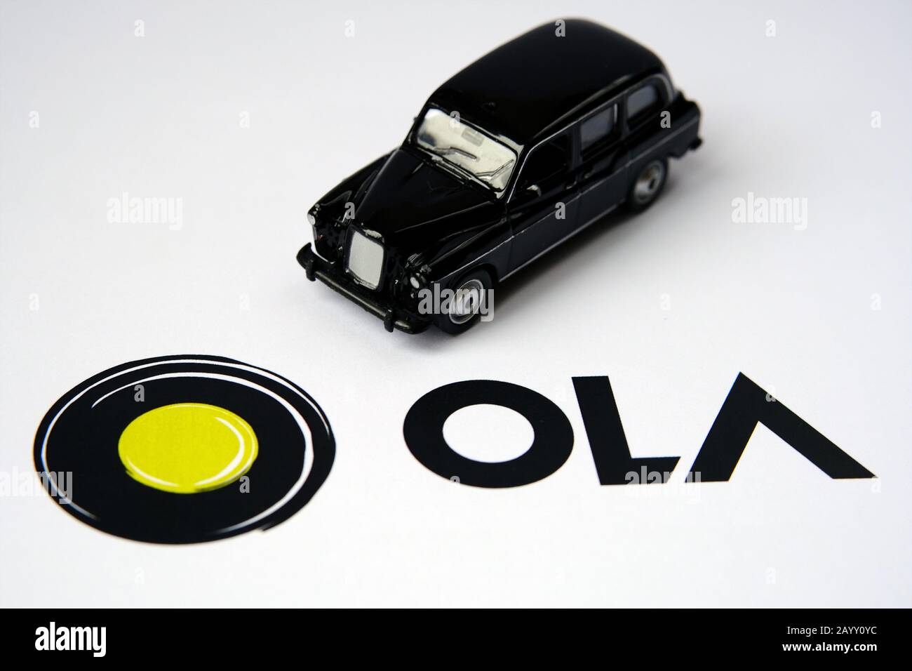 Logotipo de la aplicación Ola en un folleto en papel y cabina negra sobre fondo difuminado. Ola Cabs es una compañía de viajes compartidos. Enfoque selectivo. Foto de stock