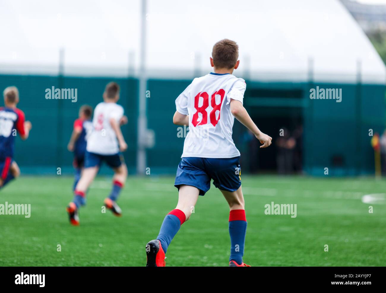 Los chicos de ropa deportiva blanca y azul juegan al fútbol en el campo,  pelota de dribles. Jóvenes jugadores de fútbol con pelota sobre hierba  verde. Entrenamiento, fútbol l Fotografía de stock -