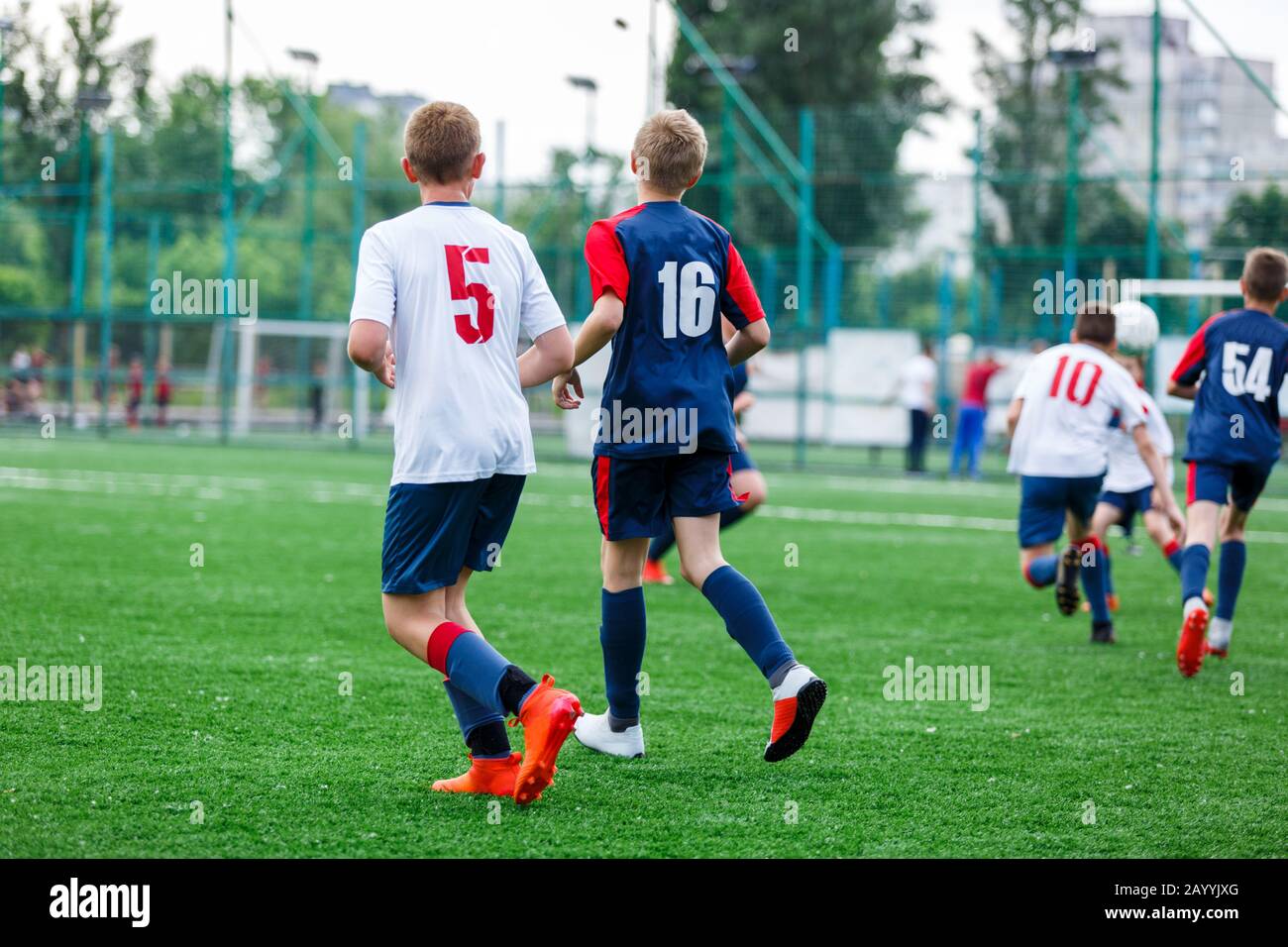 Los chicos de ropa deportiva blanca y azul juegan al fútbol en el campo,  pelota de dribles. Jóvenes jugadores de fútbol con pelota sobre hierba  verde. Entrenamiento, fútbol l Fotografía de stock -