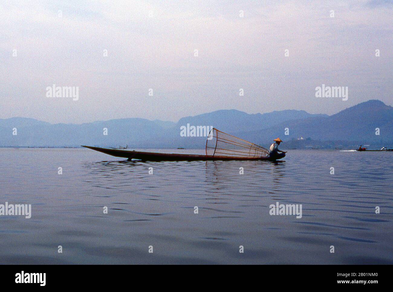 Birmania/Myanmar: Un pescador Intha en su barco en el lago Inle, en el estado de Shan. El lago Inle es un lago de agua dulce situado en el municipio de Nyaungshwe del distrito de Taunggyi del estado de Shan, parte de las colinas de Shan en Myanmar (Birmania). Es el segundo lago más grande de Myanmar con una superficie estimada de 44,9 millas cuadradas (116 km2), y uno de los más altos a una altitud de 2.900 pies (880 m). Los habitantes del lago Inle (llamado Intha), unos 70.000 de ellos, viven en cuatro ciudades que bordean el lago, en numerosos pueblos pequeños a lo largo de las orillas del lago, y en el lago mismo. Foto de stock