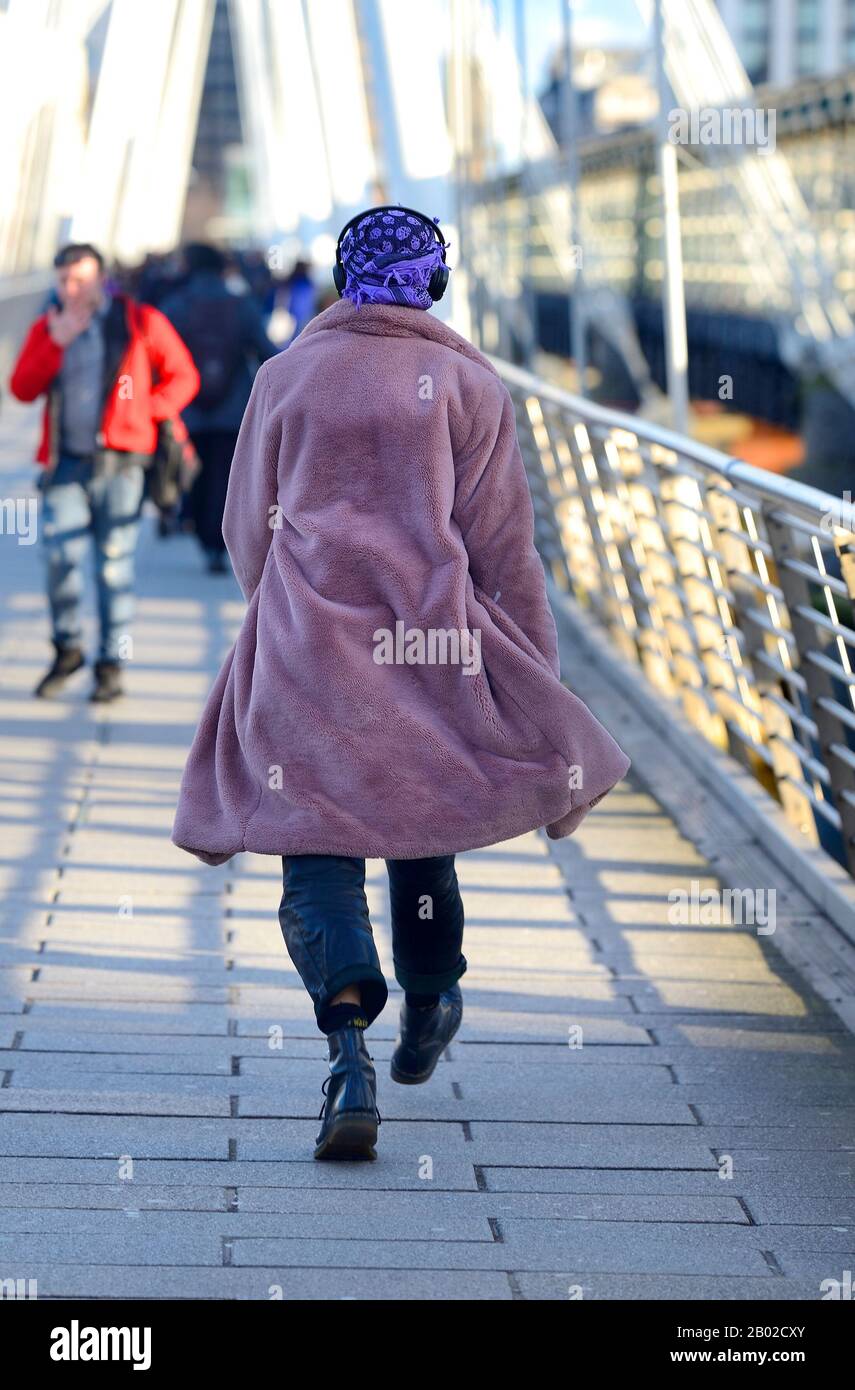 Londres, Inglaterra, Reino Unido. Hombre en un pañuelo púrpura, auriculares y bata cruzando el puente de Jubliee Foto de stock