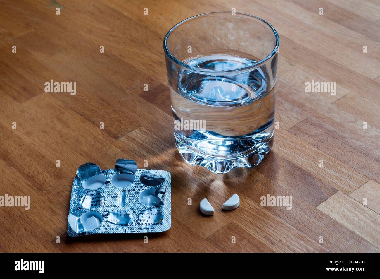 La tableta del analgésico se rompió por la mitad para administrar la mitad de la dosis, en la mesilla de noche con un vaso de agua. Foto de stock