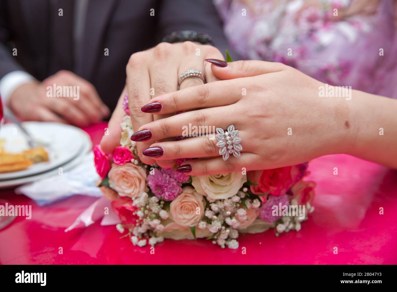 Novia y novio con anillos de oro compromiso puestos en la mesa, y junto a  ellos se encuentra un ramo de boda . mesa roja . Flores de boda coloristas  Fotografía de