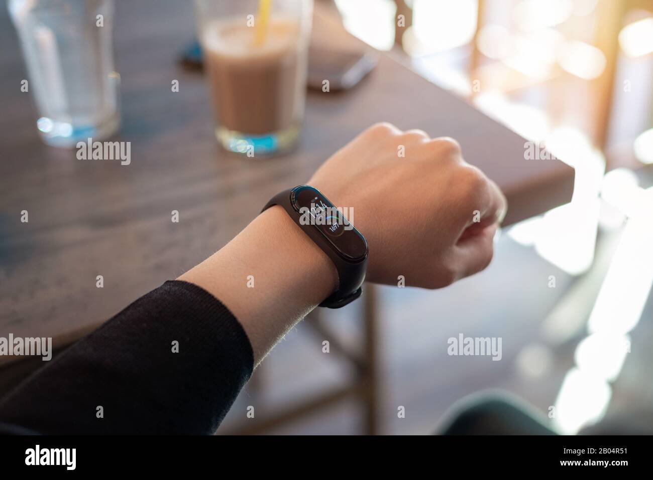 Correa inteligente en la muñeca de la mujer. Cafetería en el fondo Foto de stock