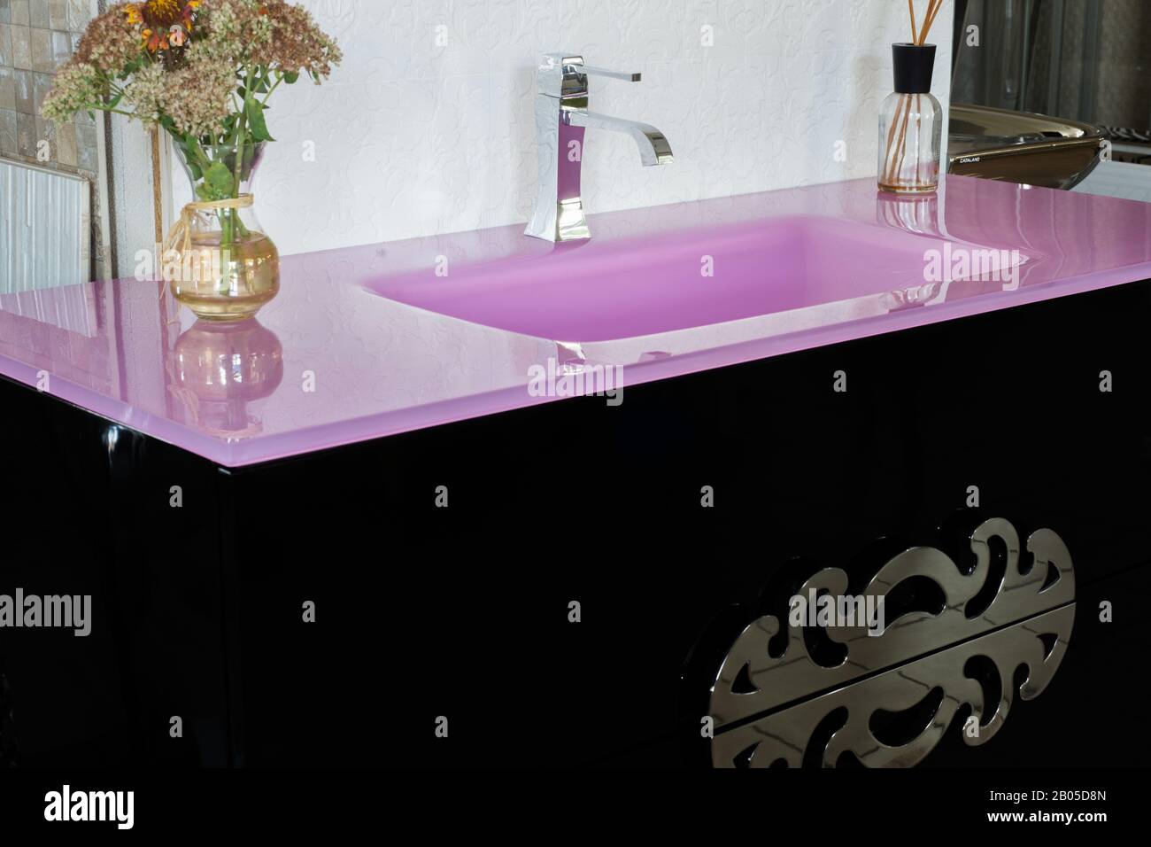 Un lavabo de piedra rosa brillante, en un interior moderno, con una mesita  de noche en negro, con una empuñadura de diseñador, con flores. lavabo en  la bathro Fotografía de stock -