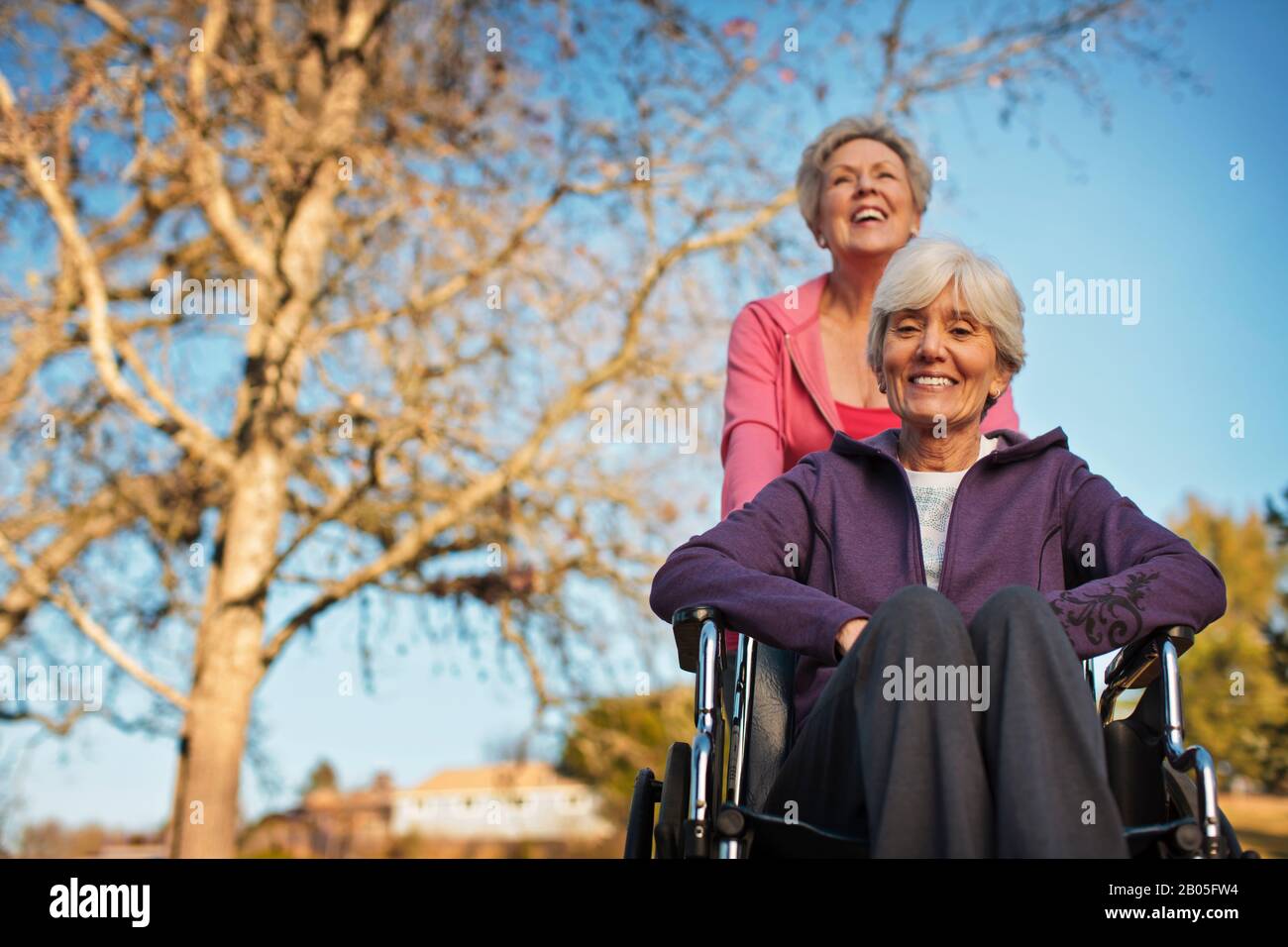 Mujer mayor en silla de ruedas siendo empujada por su hija. Foto de stock