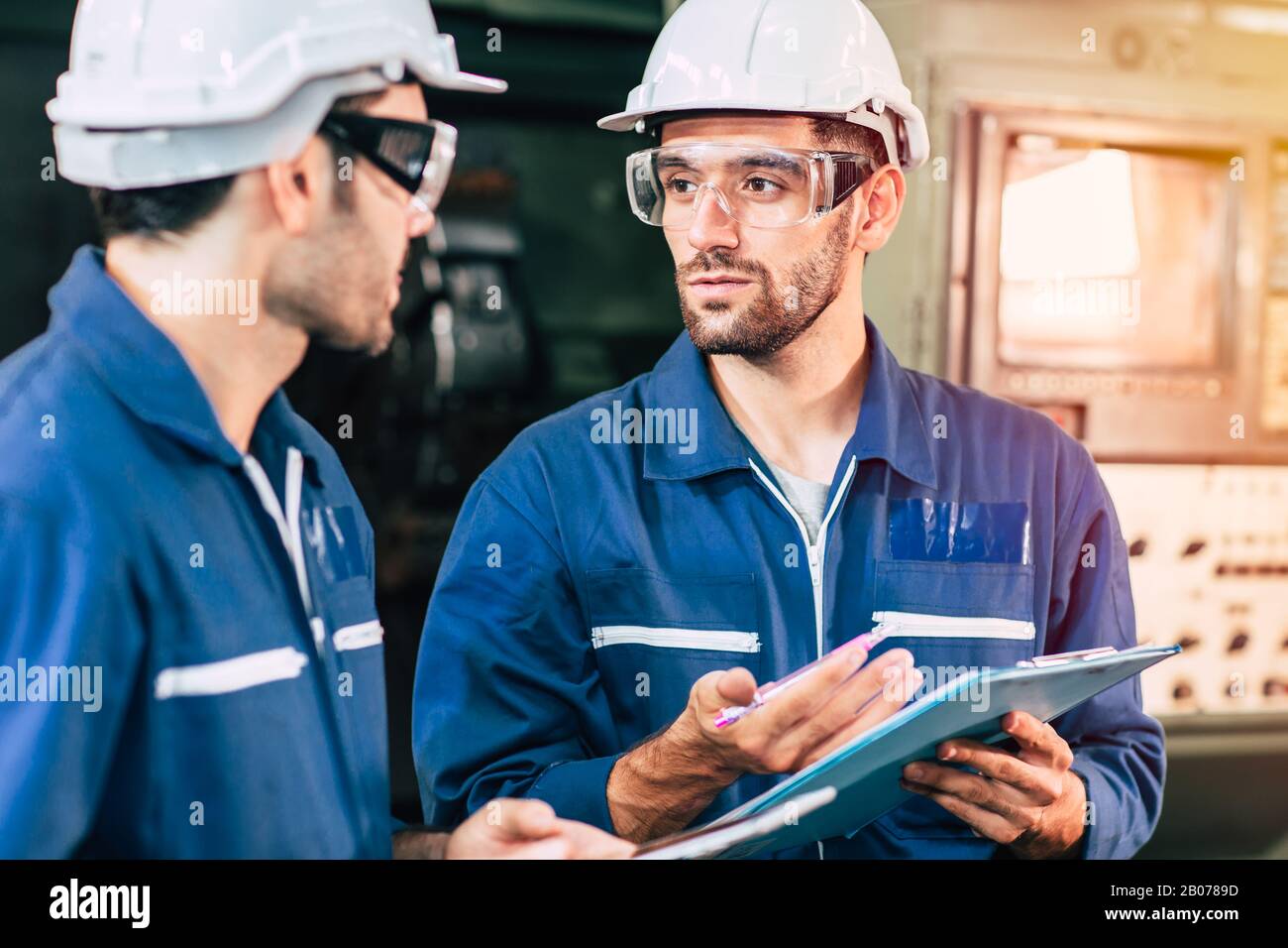 El trabajo en equipo del ingeniero coopera con el trabajador para comprobar la seguridad de la máquina de la fábrica y hablar juntos. Foto de stock