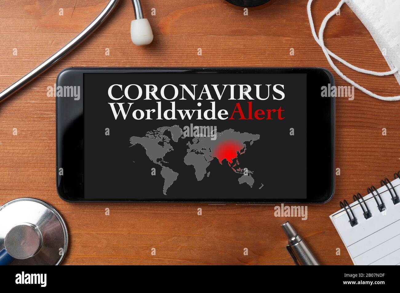 Concepto de coronavirus: Un smartphone rodeado por un estetoscopio, una máscara médica y otros objetos con un mapa del mundo y un texto de alerta en pantalla Foto de stock