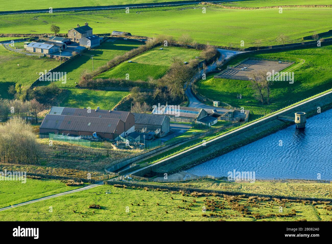 Alta vista rural soleada de campos agrícolas, muro de terraplén, presa, torre de válvulas y obras de tratamiento de agua en Embsay Reservoir - North Yorkshire, Inglaterra, Reino Unido. Foto de stock
