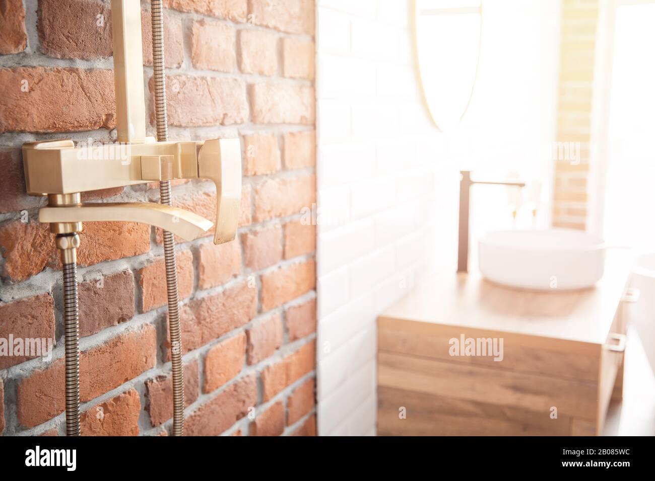 Moderno sistema de ducha de color cobre para el baño en estilo loft, pared de ladrillo. Ventana de luz solar Foto de stock