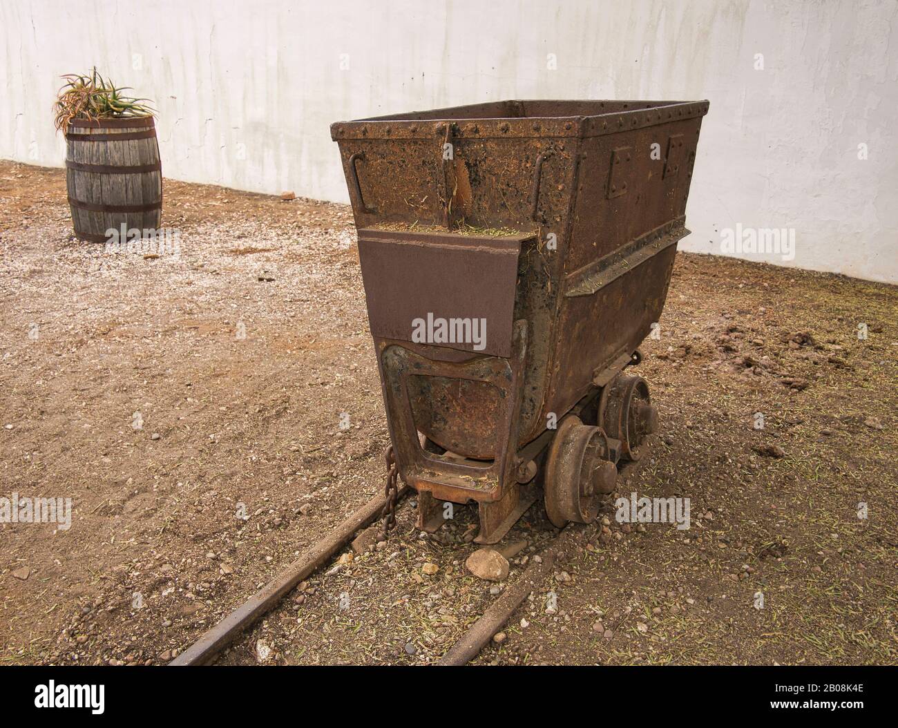 Un viejo carro minero oxidado en los rieles como decoración en el jardín Foto de stock
