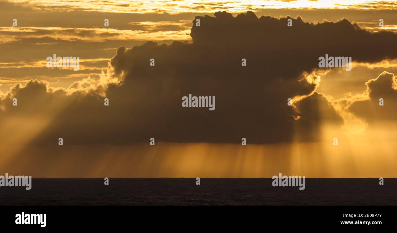 Los rayos crepusculares del sol que pone riachuelo a través de un oscuro banco de nubes monzónicas que cuelga sobre el mar de la costa en Gokarna en la India. Foto de stock