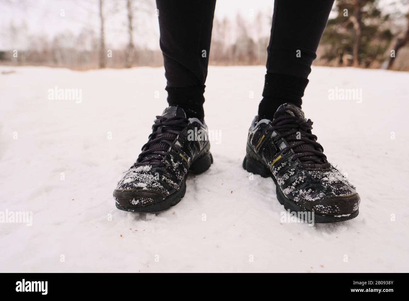 Primer plano de la persona irreconocible en invierno zapatos deportivos negros de pie sobre la nieve Foto de stock