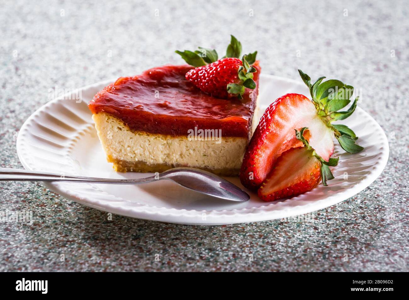 rebanada de tarta de queso con una capa de mermelada de fresa encima servida en un plato blanco con bayas frescas como guarnición Foto de stock