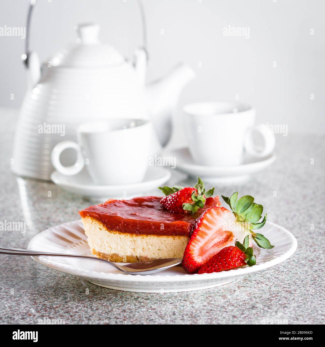 rebanada de tarta de queso con una capa de mermelada de fresa encima servida en un plato blanco con bayas frescas como guarnición Foto de stock